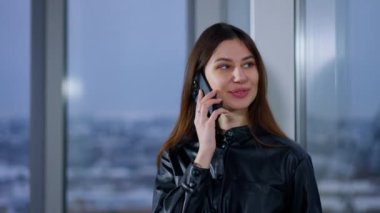 Gülümseyen kadın pencerede durup telefonda konuşuyor. Esmer iş kadını iş görüşmesi yapıyor..