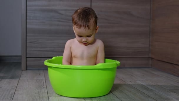 笑着的白人婴儿坐在绿色的洗脸盆里 小孩低头看了看水 然后兴致勃勃地抬起头来 — 图库视频影像