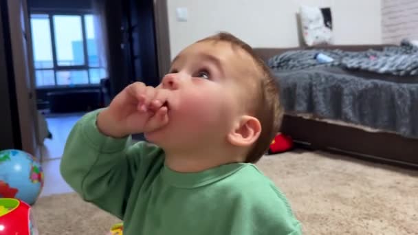 Küçük Çocuk Oyuncaklarının Yanında Yerde Oturuyor Küçük Oğlan Parmağını Ağzına — Stok video
