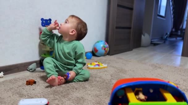 可爱的小男孩把手指伸进嘴里好奇地抬头看 可爱的孩子在屋里玩玩具 把玩具带进嘴里 — 图库视频影像
