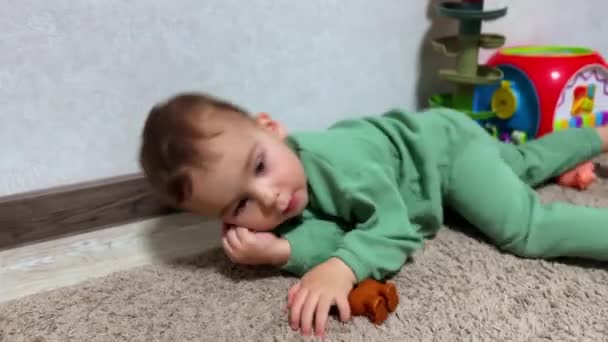 カーペットの上に横たわっている赤ん坊の少年は すぐに膝の上に立って見上げます 部屋でおもちゃで遊んでいる小さな子供 — ストック動画