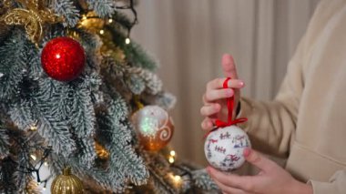 Genç çocuk elinde Noel ağacı için güzel bir balo oyuncağı tutuyor. Çocuk köknar ağacını oyuncak ve çelenklerle dekore ediyor..