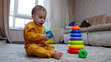 Sevimli yalınayak çocuk yerde oturmuş şişeden içiyor. Bebek şişeyi yüksekte tutuyor ve üzerine biraz su döküyor..