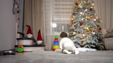 Yürüyen çocuğu takip ederek hızla yerde sürünüyorlar. Ağzında emzik olan bebek merdivenleri tırmanmayı hedefliyor. Arkaplanda Noel ağacı.