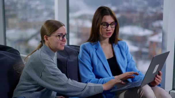 女性の同僚のコミュニケーションは ラップトップ上のファイルを議論するソフトアームチェアに座っています オフィスでの共同作業 — ストック動画