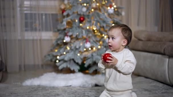 Schattige Kleine Jongen Geeft Een Mooie Rode Bal Van Kerstboom — Stockvideo
