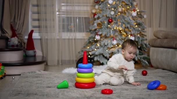 在圣诞树附近的地板上玩耍的小宝宝非常沉着 可爱的幼儿收集玩具金字塔 — 图库视频影像
