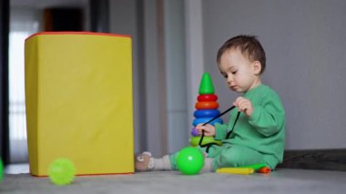Beyaz bebek, sarı oyuncak kutusunun önünde yerde oturuyor. Güzel çocuk siyah dantelle oynuyor..