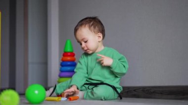 Yerde oturan güzel erkek bebek bir emzik fark etti ve hemen kaptı. Küçük çocuk dördünün de üzerinde duruyor, odanın yanında emeklemek için..