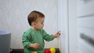 Dolabın önünde yerde oturan meraklı çocuk. Bebek kapıyı çeker ve içeri bakar..