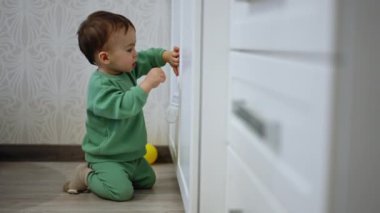 Yeni yürümeye başlayan çocuk dizlerinin üstünde dolabı açmaya çalışıyor. Çocuk düşer, ağlar ve tekrar dener..