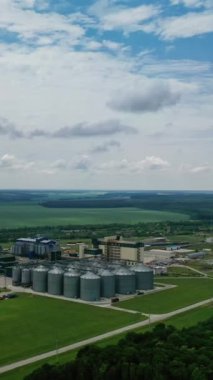 Sahada tahıl asansörleri olan sanayi fabrikası. Güzel doğa manzarasının arka planında tarım hasat deposu var. Hava görüntüsü. Dikey video