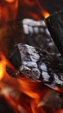 Kamp ateşinde odun yakmak. Yanan siyah ahşap üzerinde detaylı ateş hareketi. Parlak alevlerin içindeki tahta kütükler. Yakın plan. Dikey video