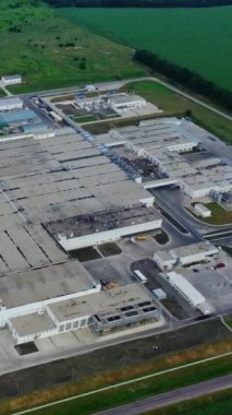 Sanayi kompleksi. Üretim binalarının çatılarından manzarayı izle. Yeşil alanda büyük bir fabrika. İHA iniyor. Dikey video