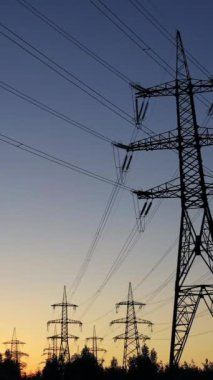 Akşamları elektrik direkleri. Gün batımında gökyüzüne karşı yüksek voltajlı elektrik hatları. Aktarım kuleleri. Alacakaranlıkta yüksek voltajlı elektrik direkleri. Dikey video
