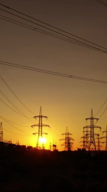 Gün batımında yüksek voltajlı elektrik hatları. Elektrik dağıtım istasyonu. Yüksek voltajlı elektrik iletim kuleleri. Kamera hareketi ileri. Dikey video
