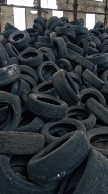 Çatı ve duvarında delikler olan yıkık dökük fabrikada büyük bir araba lastiği yığını. Eski büyük boş binanın içinde yerde bir sürü siyah lastik lastik lastik vardı. Hareket kamerası aşağı yukarı. Dikey video