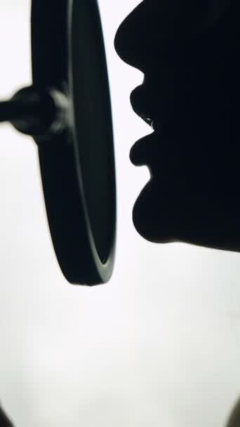 可爱的女人在录音室对着话筒唱歌 有一张漂亮的脸和嘴唇的歌手的相貌 黑色和白色 关闭垂直视频 — 图库视频影像