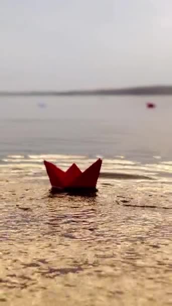 女人的手把红纸船放在水面上 让人在日落时游泳 夜间奥里加米号在河上的波浪上航行 — 图库视频影像