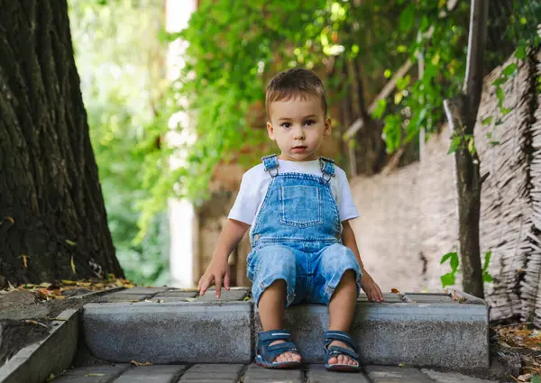 Küçük çocuk parkta merdivenlerde oturuyor..