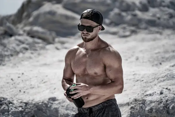 Muscular man drinking beer on the beach