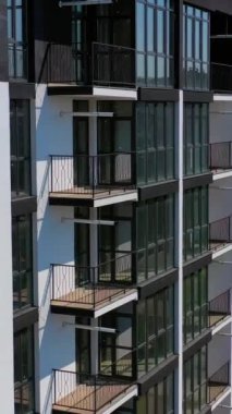 Yeni inşa edilmiş şehir mimarisi. Şehirdeki konut binasının dışında. Uzun cam pencereleri ve balkonları olan modern bir bina. Dikey video