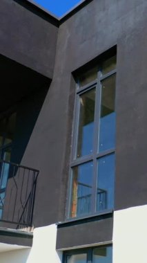Uzun siyah beyaz mimari. Balkonlu yeni konut binasının modern cephesi. Kamera yukarıdan aşağıya hareket ediyor. Dikey video