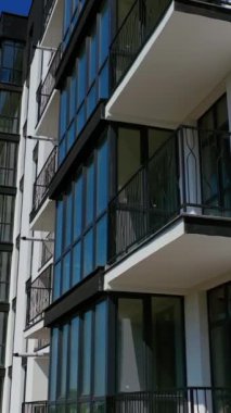 Çok katlı binanın güzel tasarımı. Mavi gökyüzüne karşı balkonları olan yeni bir daire. Konut binasının dışı. Kamera yükseliyor. Ağır çekim. Dikey video