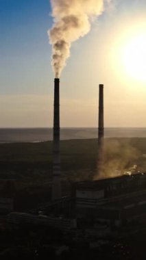 Doğa tehlikede. Nehir kenarında zararlı bir fabrika. Akşamları endüstriyel borulardan çıkan kimyasal dumanlar. Hava görüntüsü. Dikey video