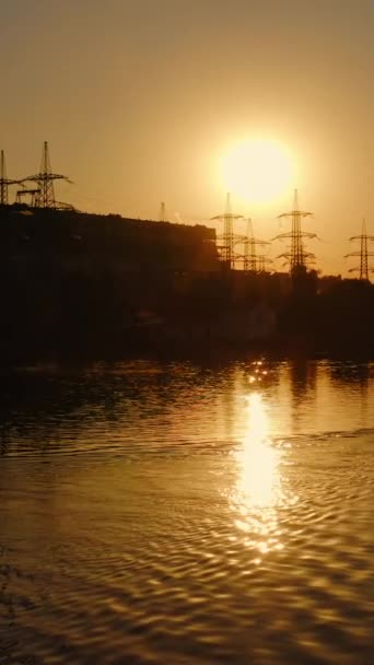 河畔一家工厂的轮廓 日落时 船里的人拿着桨散步 高压电塔靠近水面挡住落日 垂直录像 — 图库视频影像