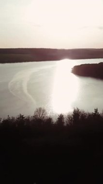 Gün doğumunda geniş ve sessiz nehir tarlalar ve ormanlar arasında yer alır. Nehrin kıyısında kırsal manzarası güzel olan küçük bir ev duruyor. Hava görüntüsü. Dikey video