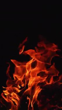 Karanlıkta dans eden şenlik ateşinin kırmızı alevleri. Geceleri yanan kamp ateşinin yakın görüntüsü. Dikey video