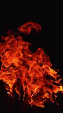 Sarı ve turuncu alevler karanlıkta hareket eder. Şenlik ateşinin üst kısmı gece yanıyor. Kapatın. Dikey video