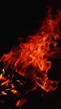 Kamp ateşinde yığılmış odun parçaları yanıyor. Geceleri yanan şenlik ateşinin ıssız manzarası. Dikey video