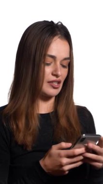 Güzel bir kadın elinde gümüş renkli bir telefonla beyaz bir odanın ortasında duruyor ve arkadaşına bir mesaj yazıyor. Dikey video