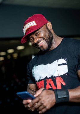 Vücut geliştiren adam telefonla poz veriyor. Spor salonunda tişörtlü güçlü bir genç..