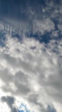 Beyaz pamuk bulutları hızla gökyüzünde uçuyor. Mavi ve güneşli gökyüzünün arka planında ağır bulutlar. Aşağıdan bak. Dikey video
