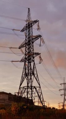 Gün batımında yüksek voltajlı elektrik kuleleri. Akşam arkaplanındaki iletişim hatları. Elektrik dağıtımı. Aşağıdan bak. Dikey video