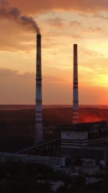 Doğadaki kimyasal bitki. Gün batımında fabrikadan kirli duman çıkıyor. Zararlı emisyonlara sahip endüstriyel boru çevreyi kirletir. Hava görüntüsü. Dikey video