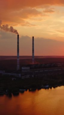 Nehir kenarındaki bir kimya fabrikasının silueti. Endüstriyel fabrika güzel gün batımında duman salıyor. Doğada tehlikeli imalat. Hava görüntüsü. Dikey video