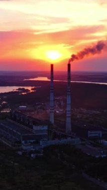 Ekolojik felaket. Nehir kenarındaki zararlı fabrika gün batımında kirli salınımları serbest bırakıyor. Endüstri çevreyi kirletir. Güzel bir arka planda dumanı olan borular. Dikey video