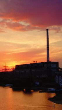 Gün batımında pembe gökyüzüne karşı zararlı bir fabrika. Endüstriyel bacadan çıkan duman çevreyi kirletiyor. Akşam nehrinin yanındaki kimyasal tesiste. Dikey video