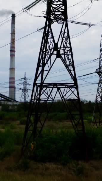 高压电塔 输电线路以工业厂房为背景 农村田里的钢制电塔 摄像头升起了 垂直录像 — 图库视频影像