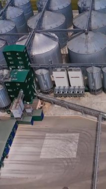 Sahadaki tahıl asansörü bolluğu. Sıraya dizilmiş metal ambar tanklarının üzerinde uçuyorlar. Havadan bakış açısı. Dikey video