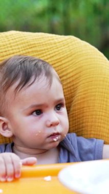 Yemek masasında yemek yiyen sevimli bir çocuk. Sevimli çocuk annesinin eline bakar tabaktan çıkan lapayla kaşığı doldurur. Kapatın. Arkaplan bulanık. Dikey video