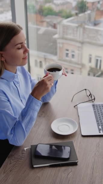 金发女人坐在写字台前 手里拿着一杯咖啡 放松的女士在工作场所享受午餐时间 高角镜 垂直录像 — 图库视频影像