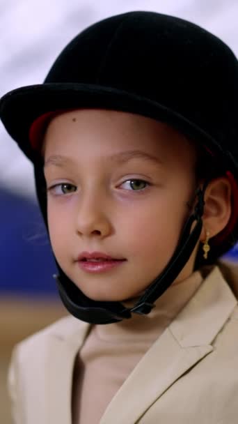 可爱的小孩戴着大大的黑色骑师头盔女孩在镜头前微笑着触摸着帽子 与逐渐疏远的亲密接触 模糊的背景 垂直录像 — 图库视频影像