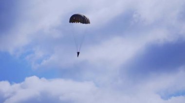 Yere paraşütle inen adamın silueti. Mavi bulutlu gökyüzünde paraşütçü.