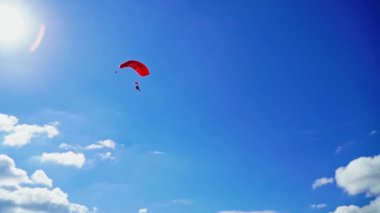 İkili kırmızı paraşüt hızla yere yaklaşıyor. İnsanlar ekstrem spor yapıyor, paraşütle atlıyor. Düşük açı görünümü.