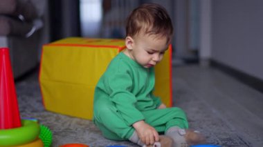 Yerde oturan bebek şişeyi düşürür ve oyuncakların dikkatini dağıtır. Tatlı çocuk içeride piramitlerle oynuyor..
